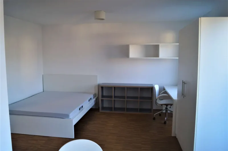 Small minimalist dorm room with a white platform bed, cube storage unit, and a white desk with a swivel chair.