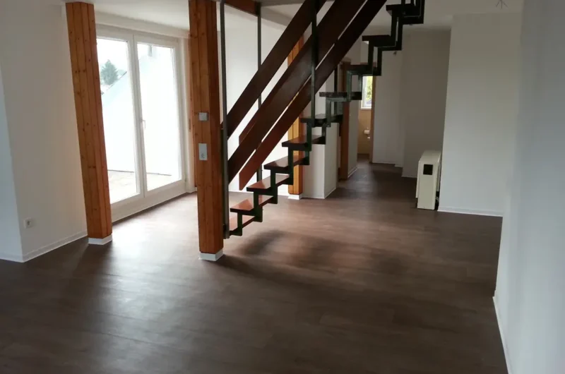Open living area with dark cantilever staircase, wooden posts, and glass doors to outdoors.