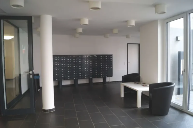 Lobby area with a row of mailbox compartments along the back wall, a white column, and black seating around a white coffee table.