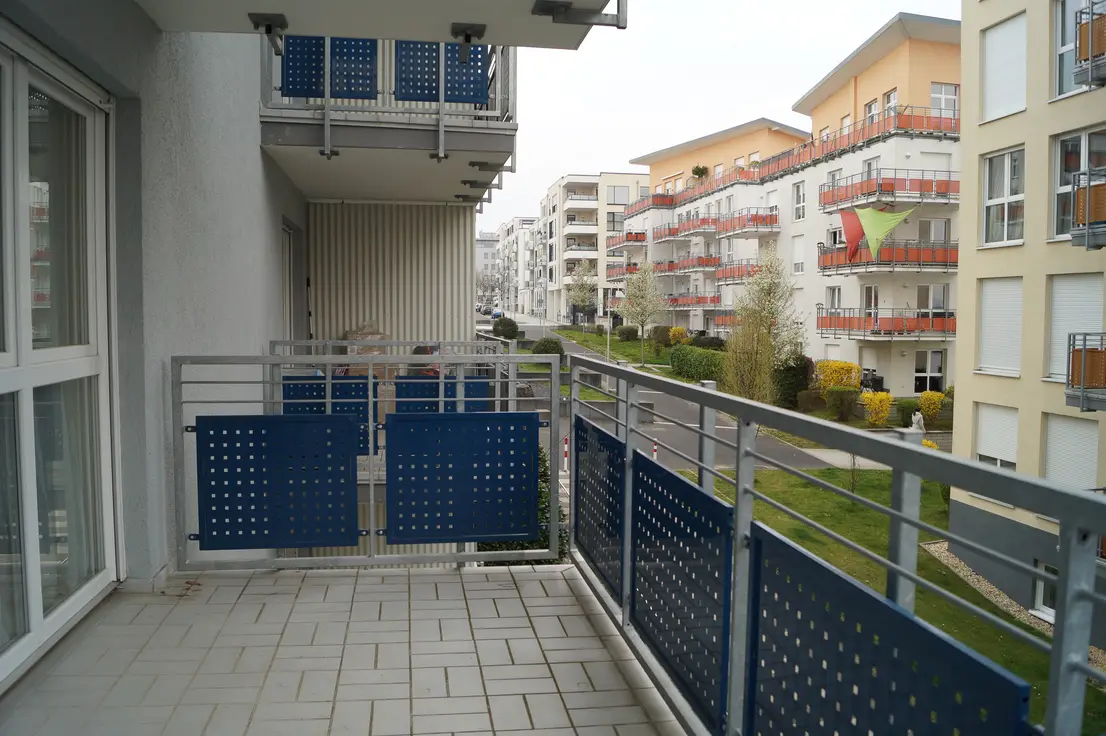 Balcony with blue perforated metal panels along the railing overlooking a row of modern apartment buildings.