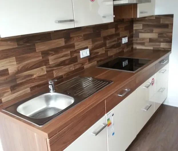 Modern L-shaped kitchen with wood countertops, white cabinets, and a stainless steel sink and stovetop on a wood-tile floor for a compact cooking space.
