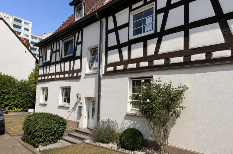 White half-timbered house with dark wooden beams, front door and small garden under a blue sky.