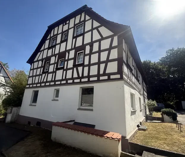 Two-story timber-framed house with white plaster and dark wooden beams on a sunny day (European-style).