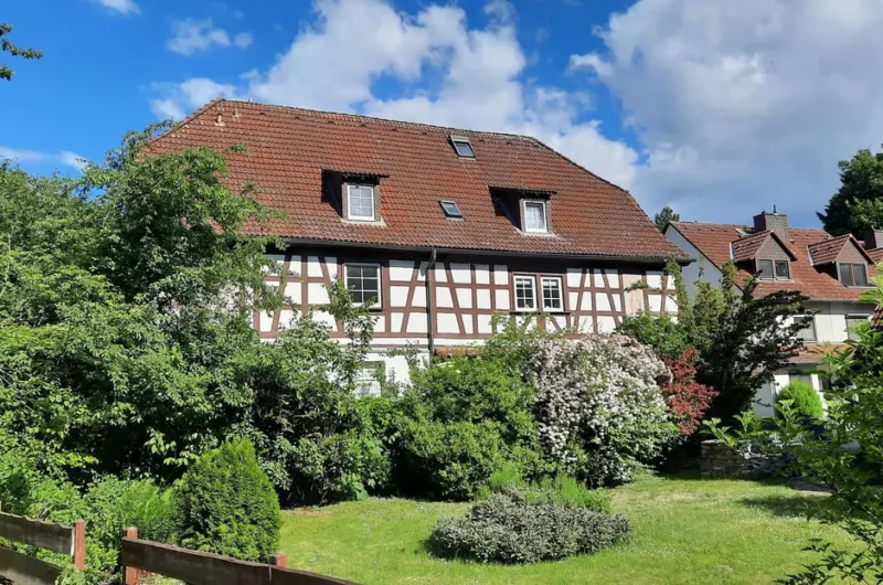 Half-timbered house with a red tiled roof, surrounded by green bushes and a manicured garden.