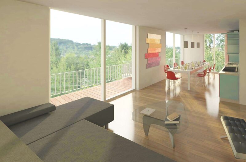 Bright open-concept living and dining area with large windows overlooking greenery; gray sofa in foreground and a white dining table with red chairs to the right, balcony railing visible outside